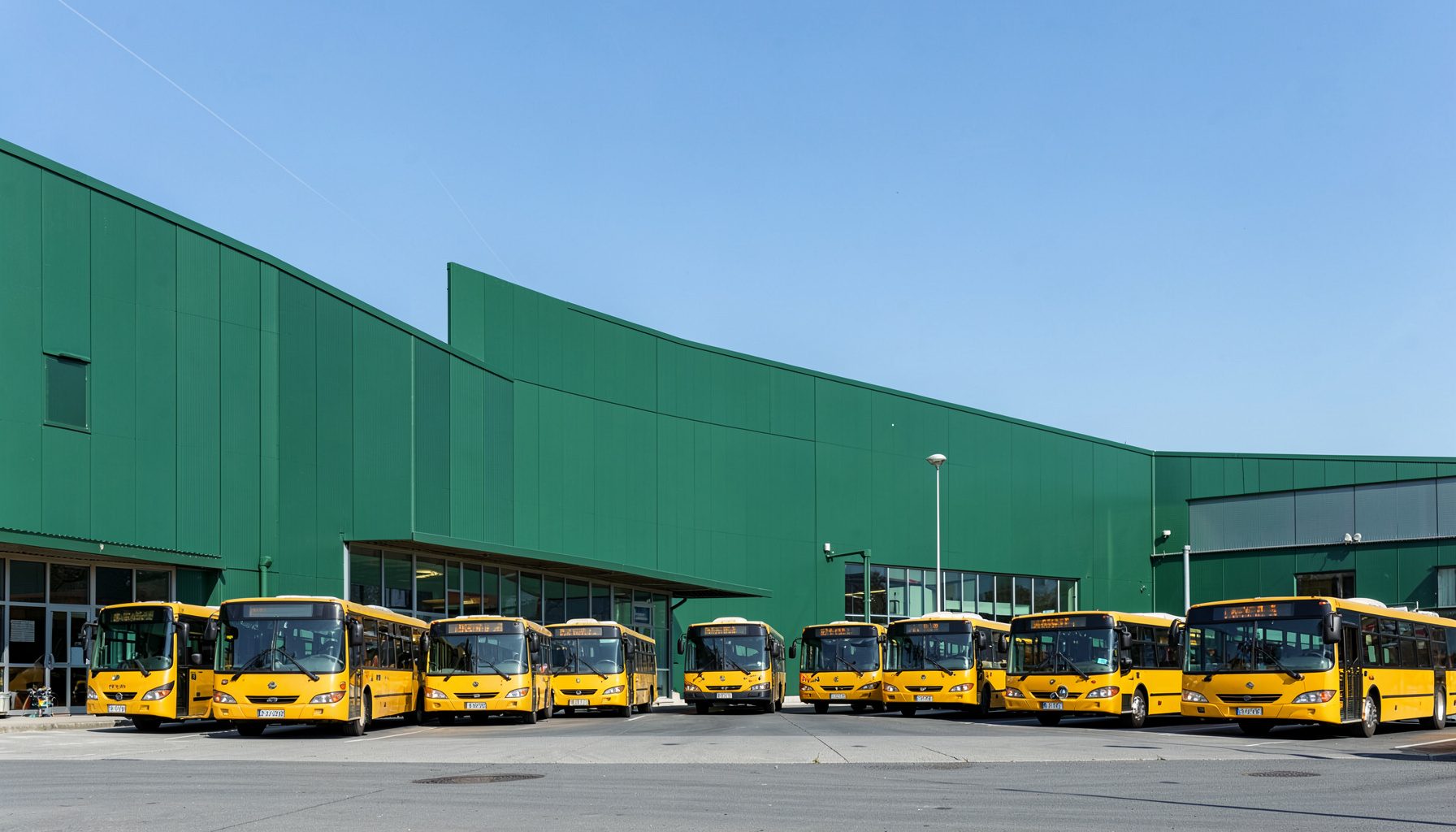 Rangée de bus scolaires jaunes alignés devant un bâtiment industriel sous un ciel clair, évoquant fiabilité et professionnalisme.