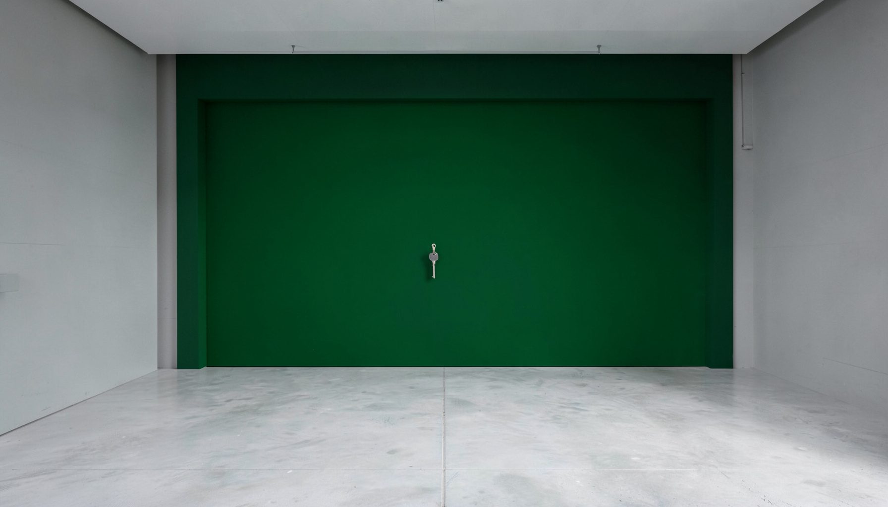 Main tendue recevant un jeu de clés, sur fond de garage propre aux lignes architecturales nettes, dans des tons gris et verts.
